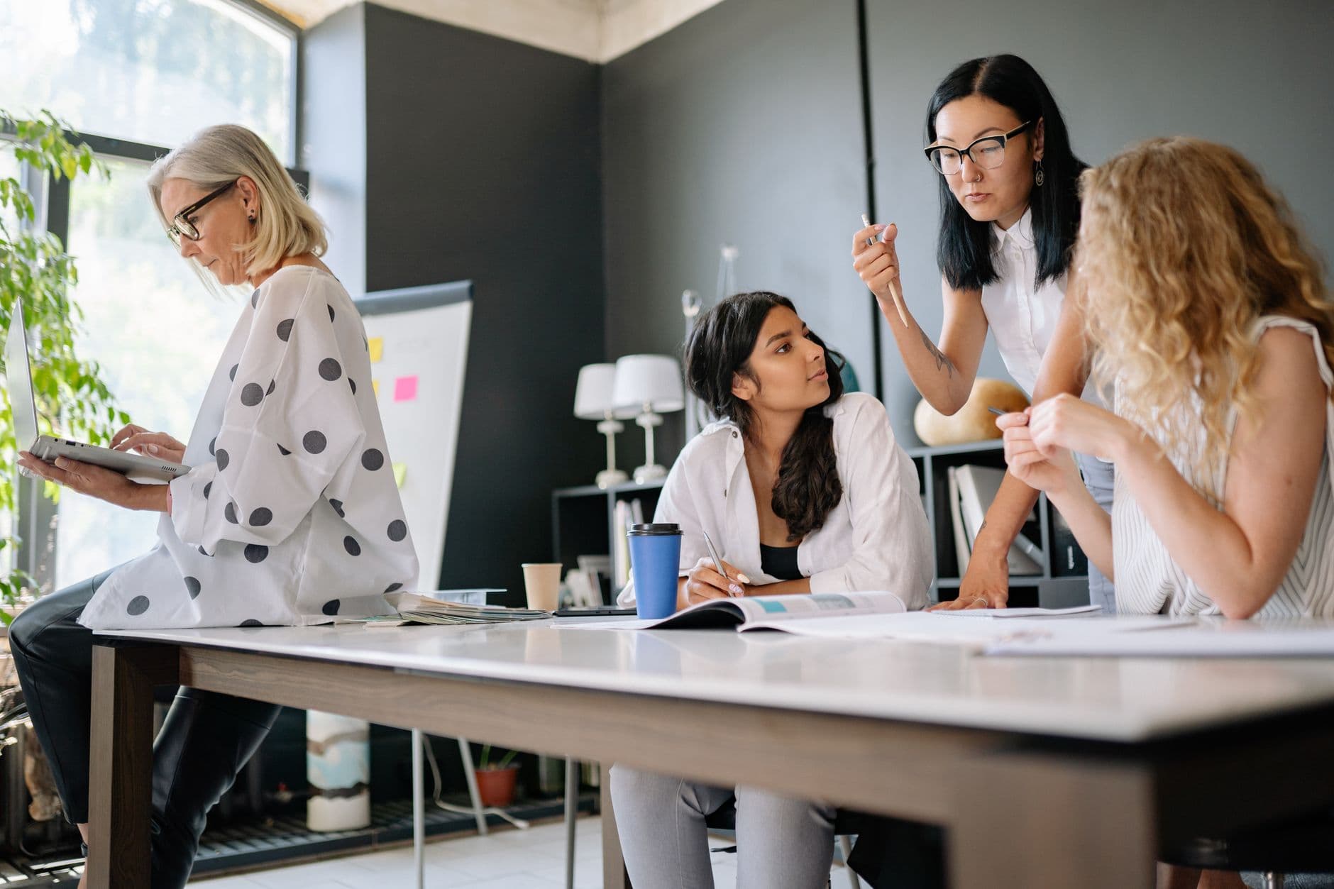 CLT híbrido: o que é e como funciona na prática A diverse group of women engaged in teamwork and discussion inside a modern office space.