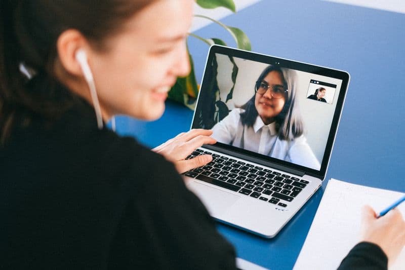 Como identificar uma vaga remota legítima no LinkedIn Woman having a video conference on a laptop, smiling and taking notes.