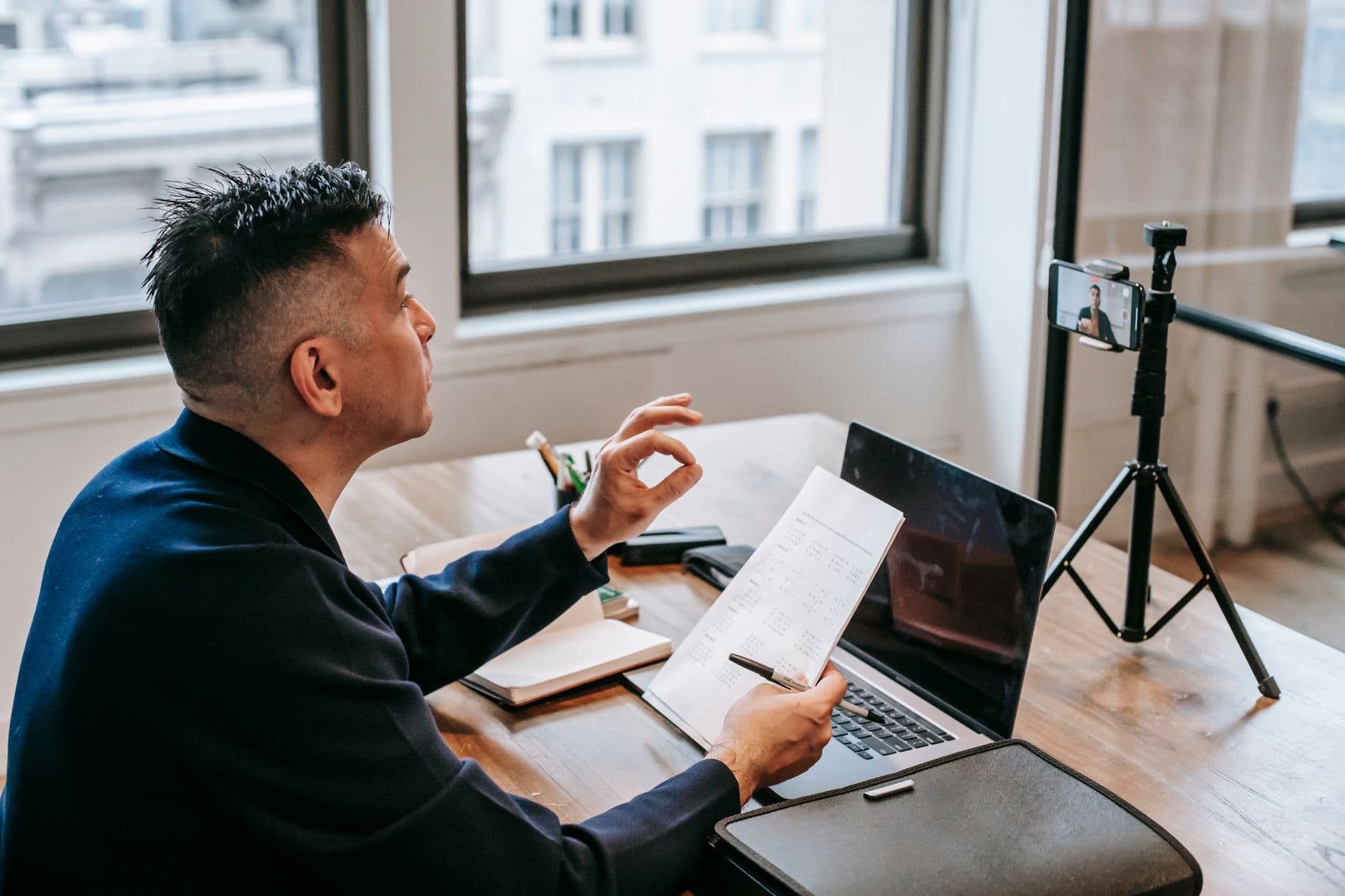 Como negociar benefícios em uma vaga remota Man using laptop and smartphone for a video call in an office setting.