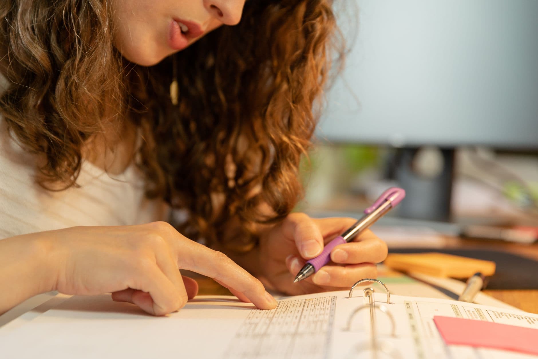 Como pedir promoção sem contato presencial Focused woman pointing and writing on paper in binder with a purple pen.