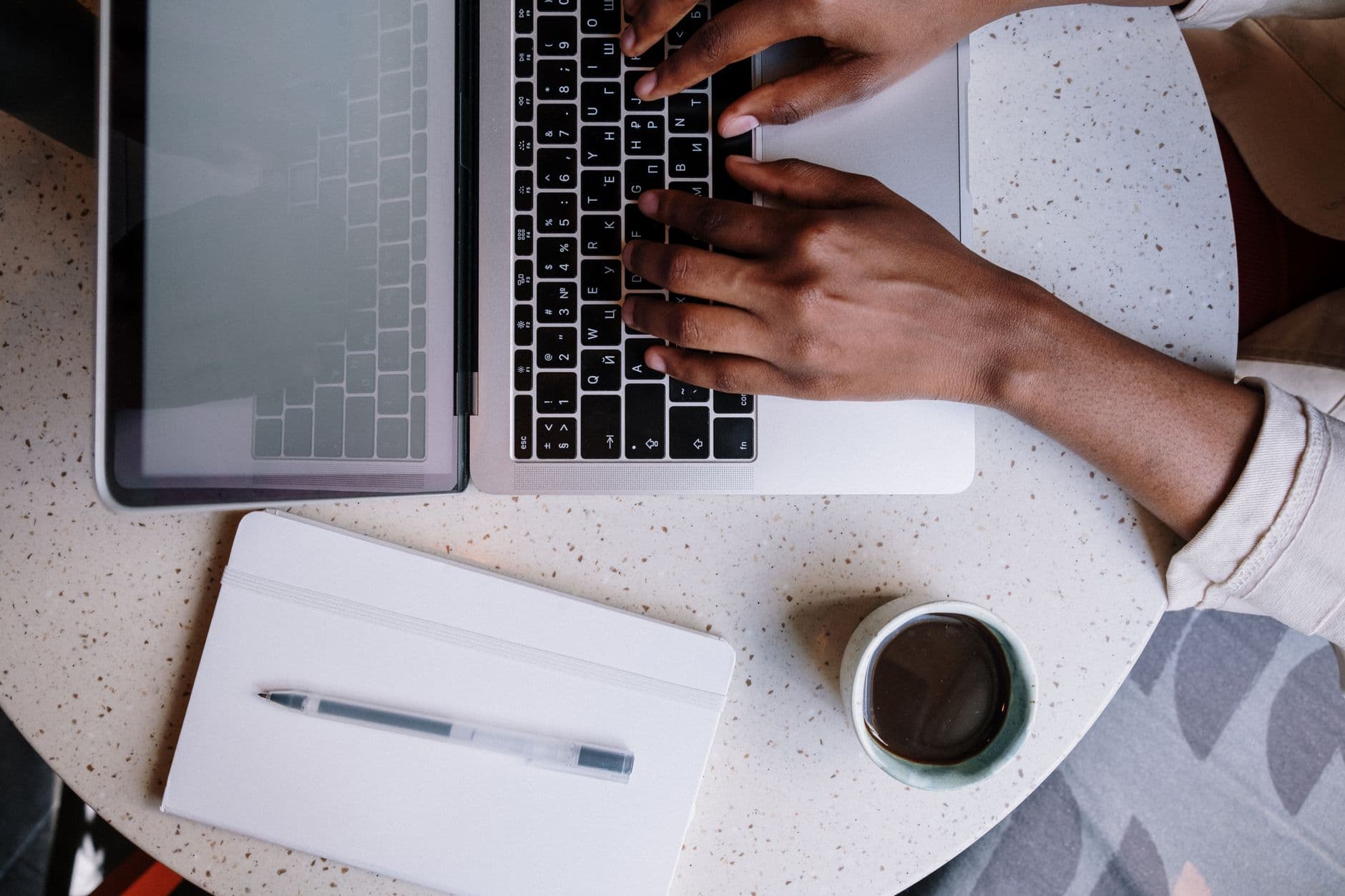 Cursos Online Gratuitos para Impulsionar a Carreira Remota Top view of a person working on a laptop in a café with a notebook and coffee, ideal for business or blogging themes.
