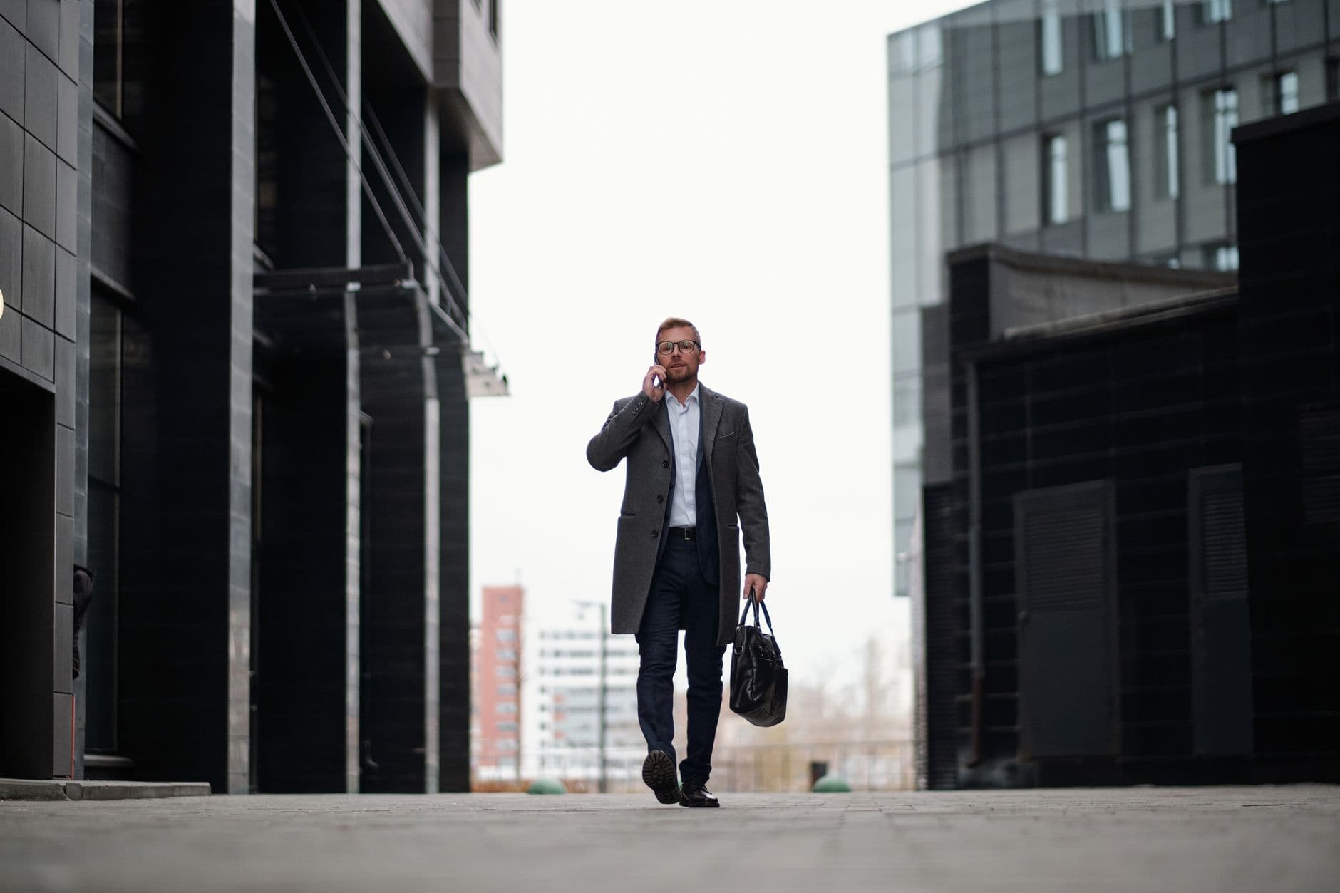 Exercícios simples para quem trabalha sentado Professional man in a suit walking outdoors, using phone in modern city.