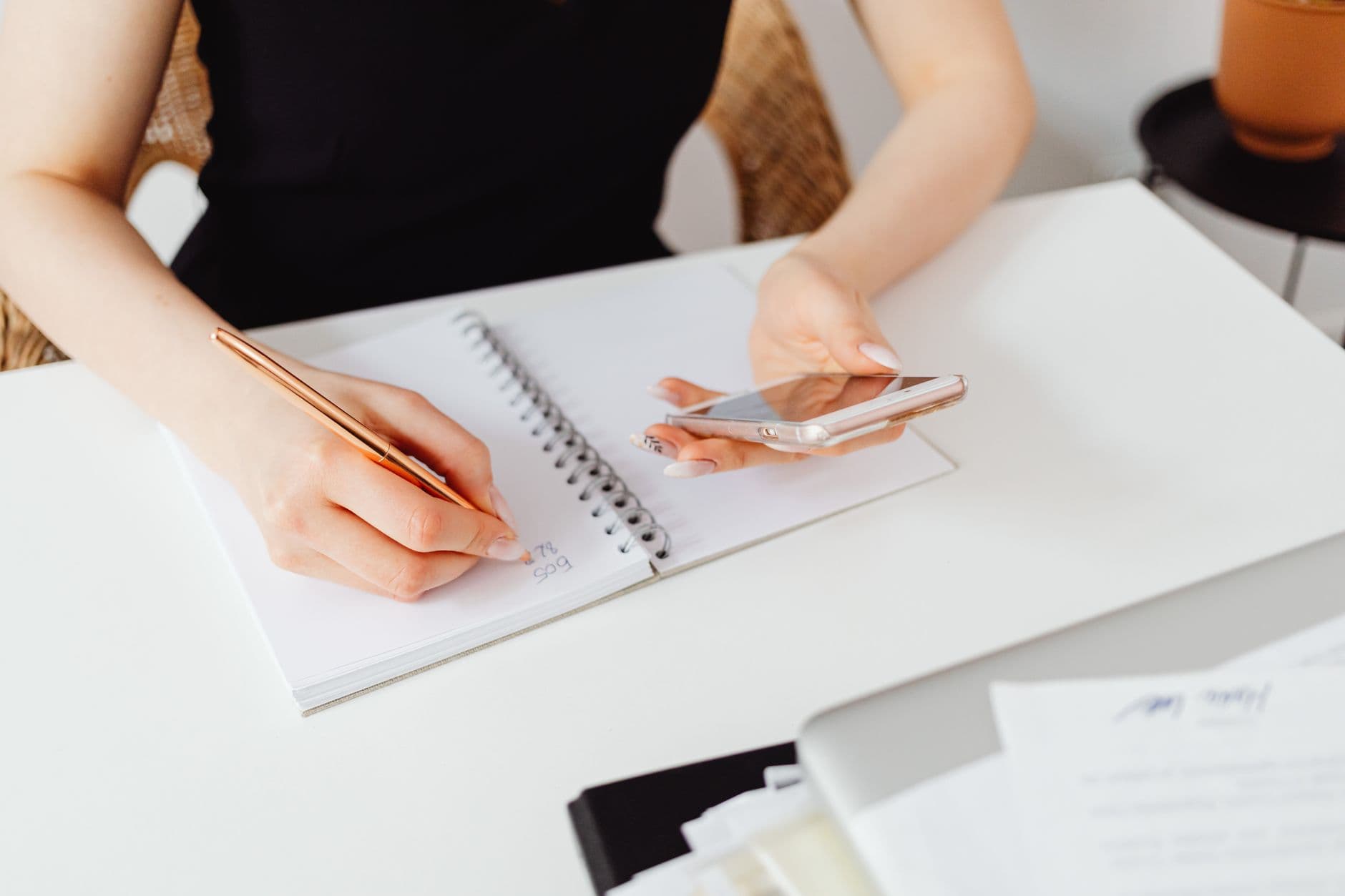 Como descobrir seu horário nobre de produtividade A woman writes in a notebook while holding a smartphone, symbolizing multitasking at work.