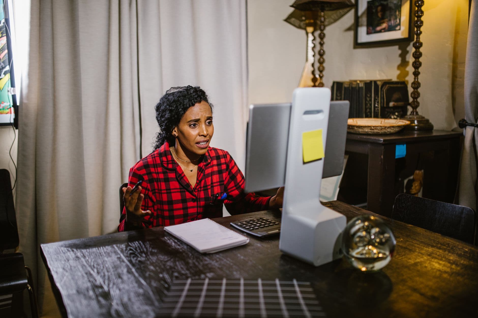 Iluminação ideal para o home office Woman in red plaid speaking at computer desk, engaged in online communication.