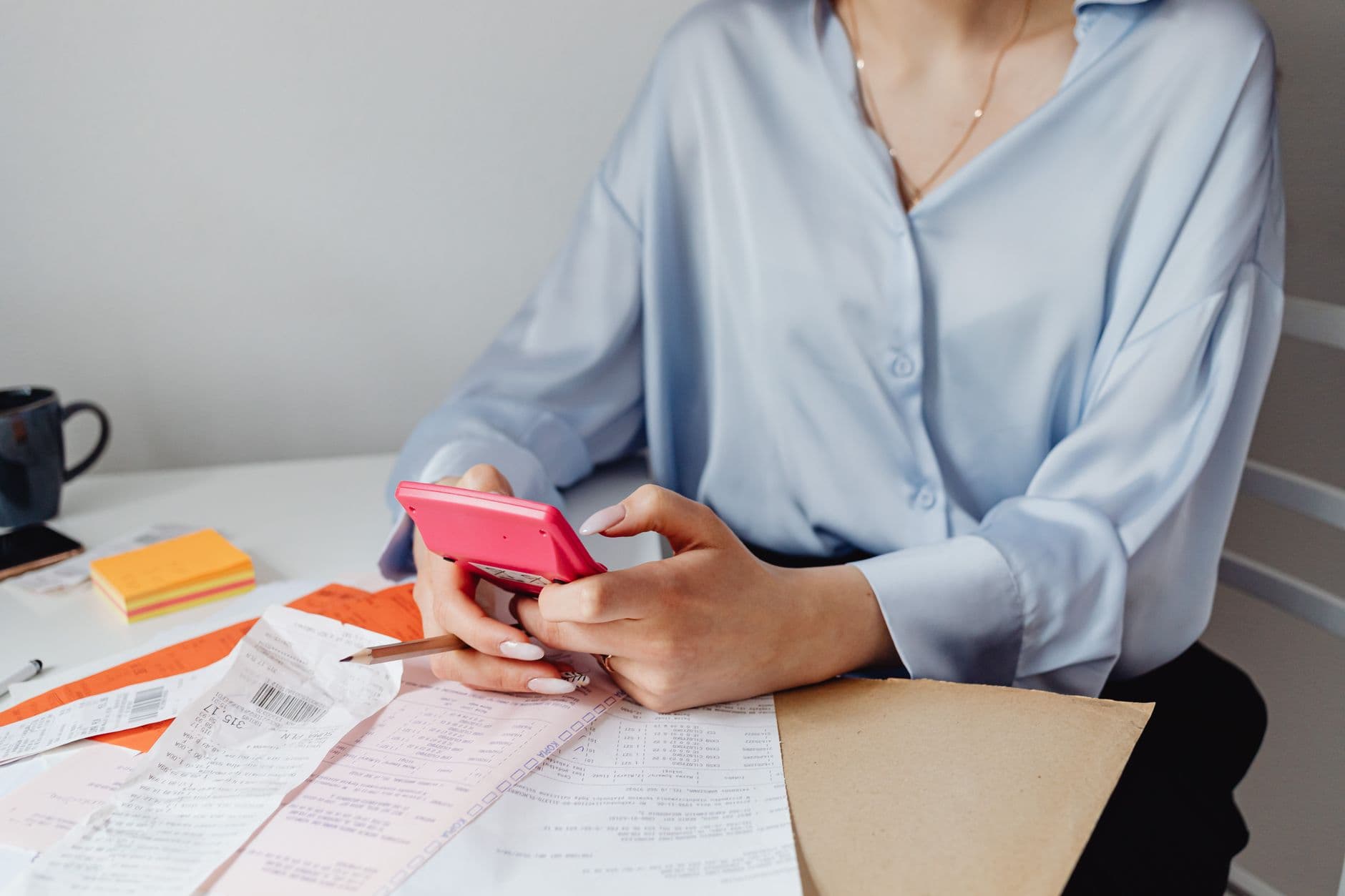 Imposto de renda para freelancer: como declarar A woman using a pink calculator surrounded by bills and receipts at a desk.