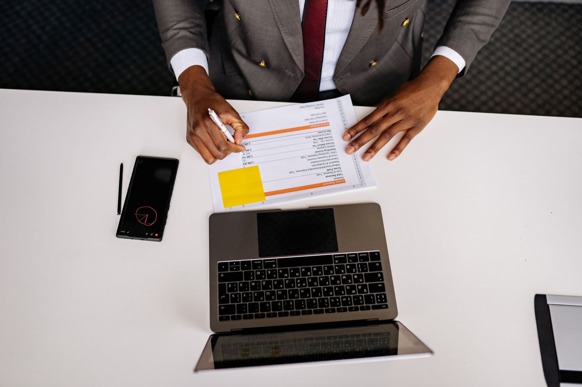 Como montar uma lista de tarefas diária no home office Top view of a business professional analyzing documents with a laptop on a white desk in an office setting.