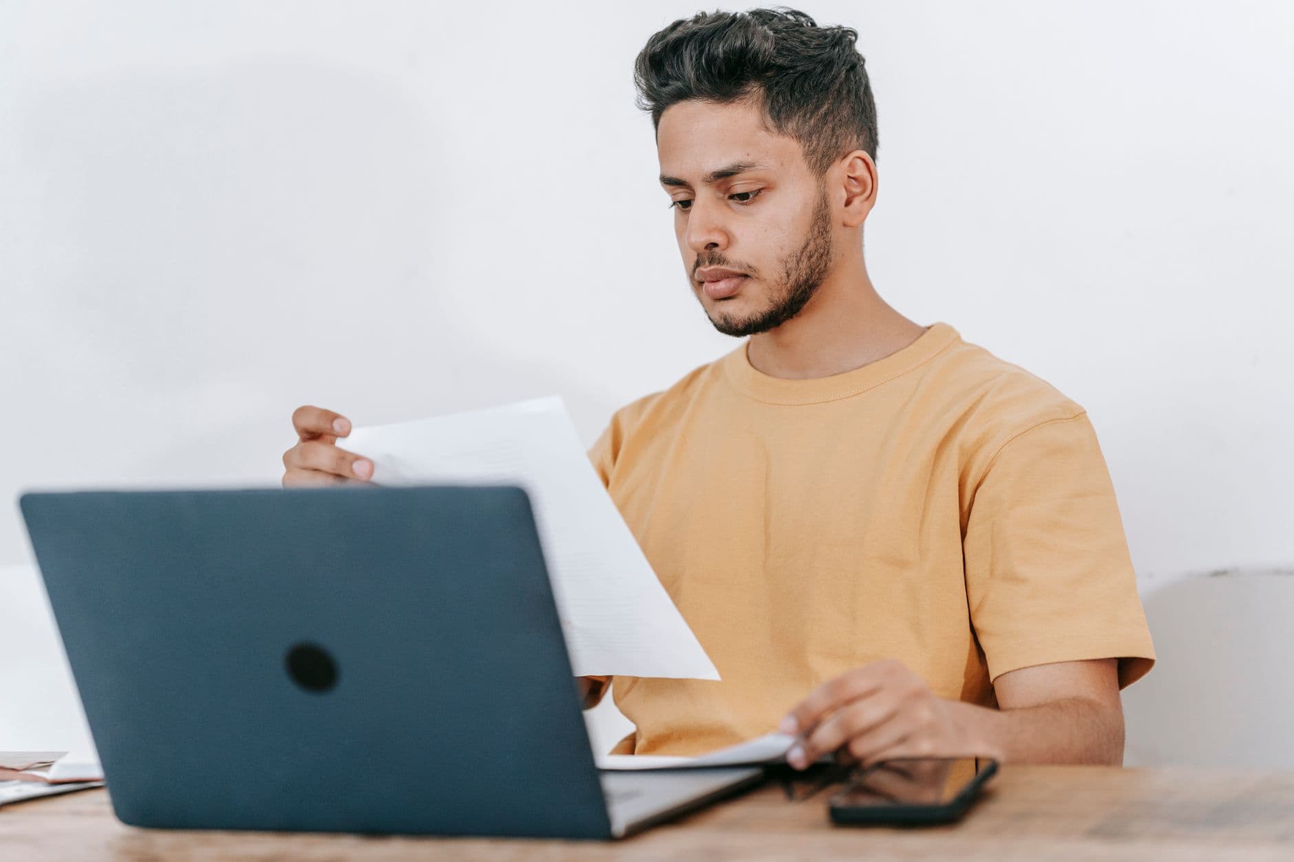 PJ ou CLT: qual compensa mais no trabalho remoto? Young bearded Hispanic male university student reading information on paper while studying online via laptop