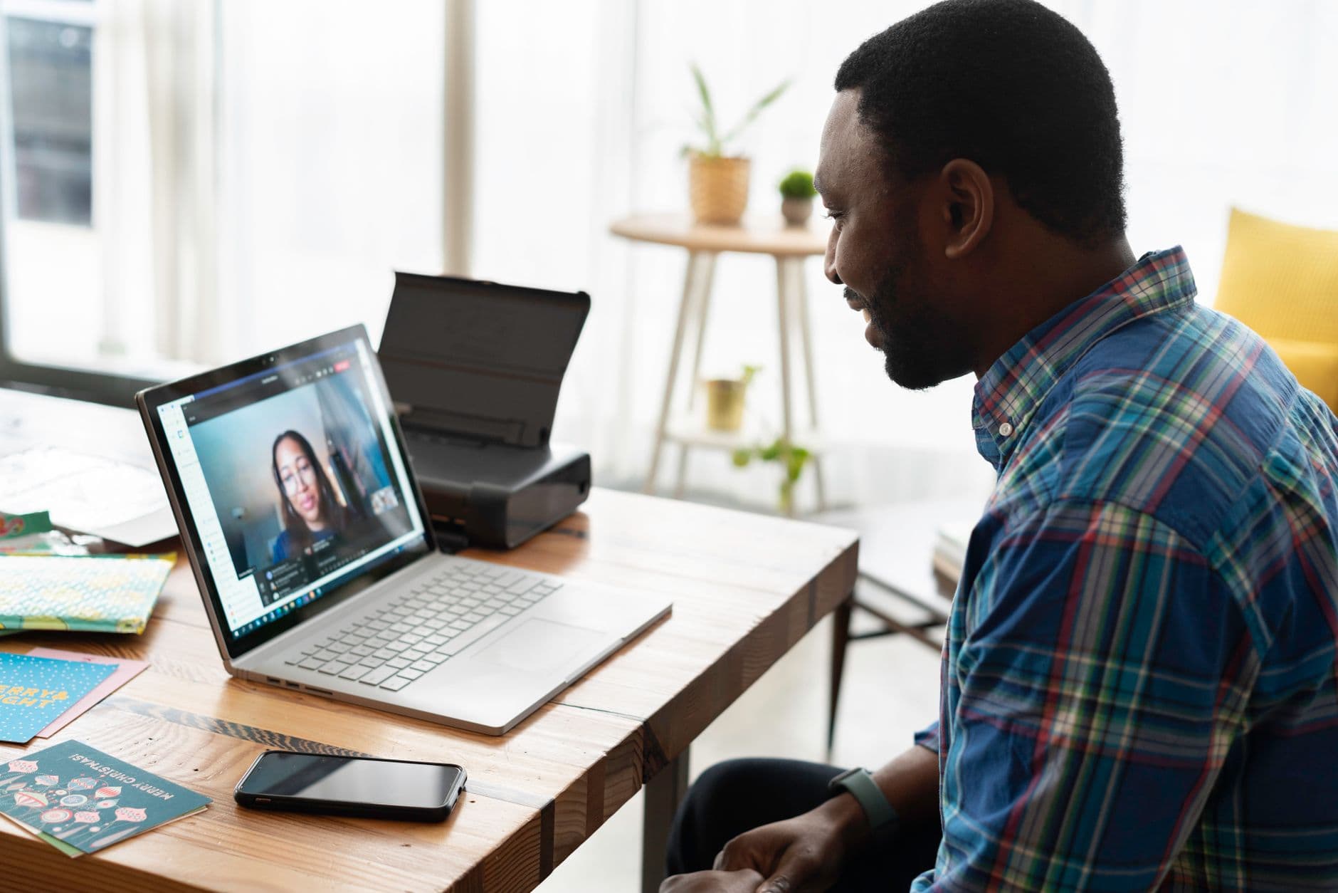 Transição de carreira para trabalho remoto: guia prático Man engaged in a video call with a colleague at a wooden desk in a modern office setting.